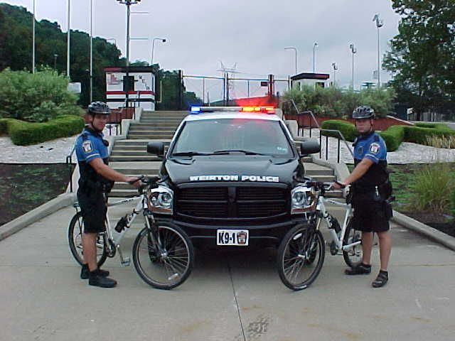 Two members of the Bicycle Patrol next to a squad car.